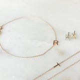 A Custom Gold Bracelet - 1 Letter with the letter R, two 14k Gold Letter Studs in H and X and a Custom Gold Necklace - 1 Letter with the letter T against a light marble background.