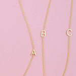Three gold necklaces with single letter charms A, B and C on a pink background. 
