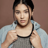 A woman wearing a dark grey top and denim jacket, a necklace with a letter W charm and stud earrings.