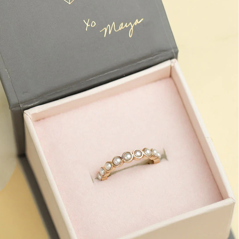 A Lily Bouquet Ring in a Maya Brenner jewelry box against a light yellow background with a painted lily.