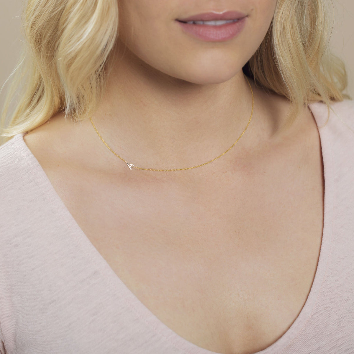 A close-up of a woman's neck wearing a gold necklace with a letter A charm. 