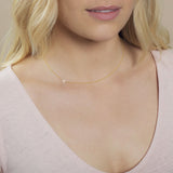 A close-up of a woman's neck wearing a gold necklace with a letter A charm. 