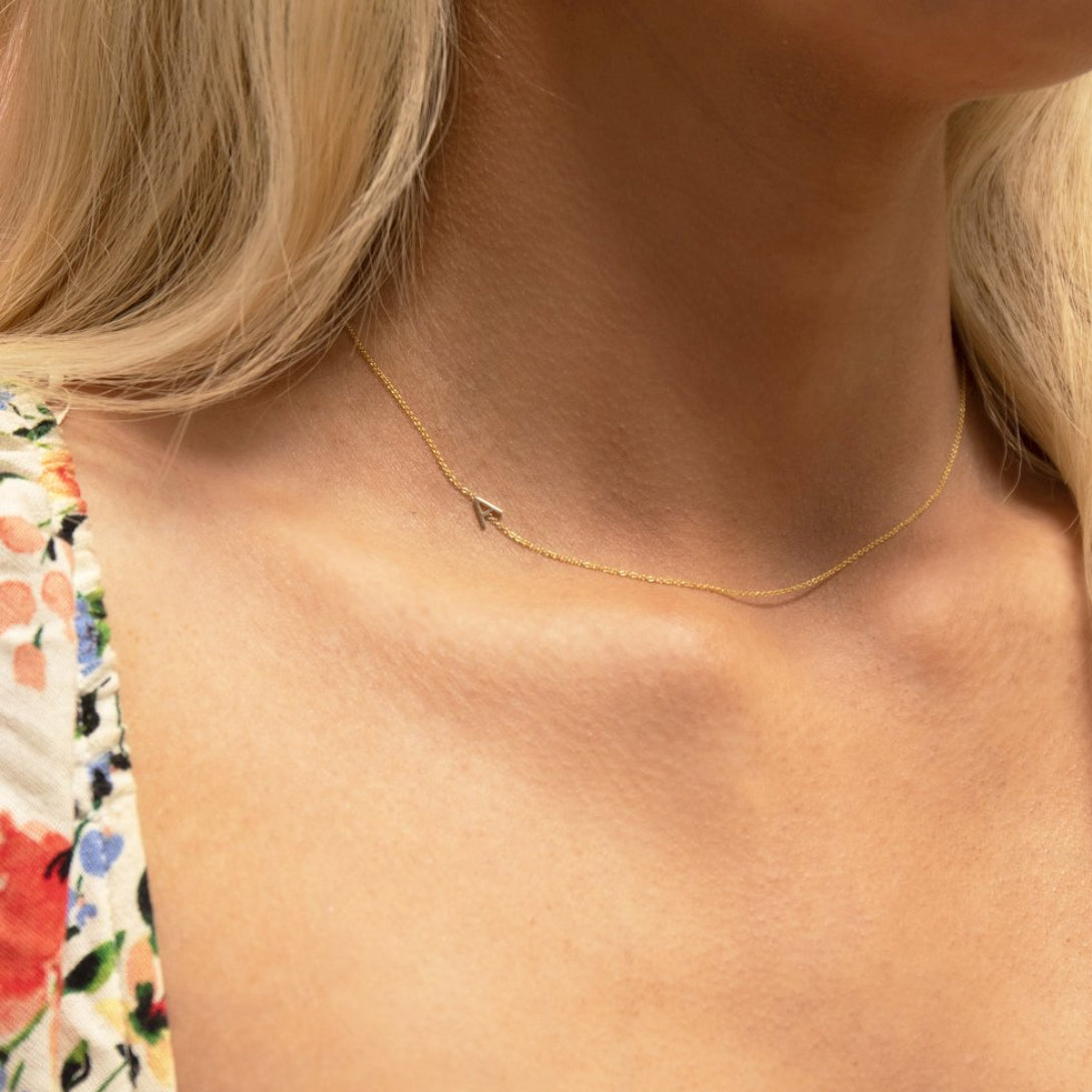 A close-up of a woman's neck wearing a gold necklace with a letter A charm. 