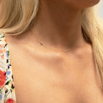 A close-up of a woman's neck wearing a gold necklace with a letter A charm. 