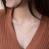 A close-up of a woman’s neck wearing two gold necklaces, one with a letter W charm and the other with the word MADRE.