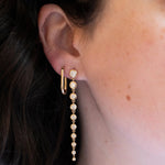 Close-up of an ear wearing an Oval Hoop and Diamond Cascade Earring in yellow gold. 