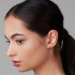 A close-up of a woman's side profile wearing two yellow gold threader earrings with letter studs M and B.