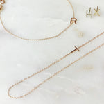 A necklace, bracelet and two stud earrings, each with its own letter charm – R, T, H, and X against an off white marble background. 