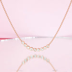 A Diamond Arc Layering Necklace in yellow gold against a light pink background. 