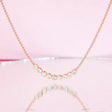 A Diamond Arc Layering Necklace in yellow gold against a light pink background. 