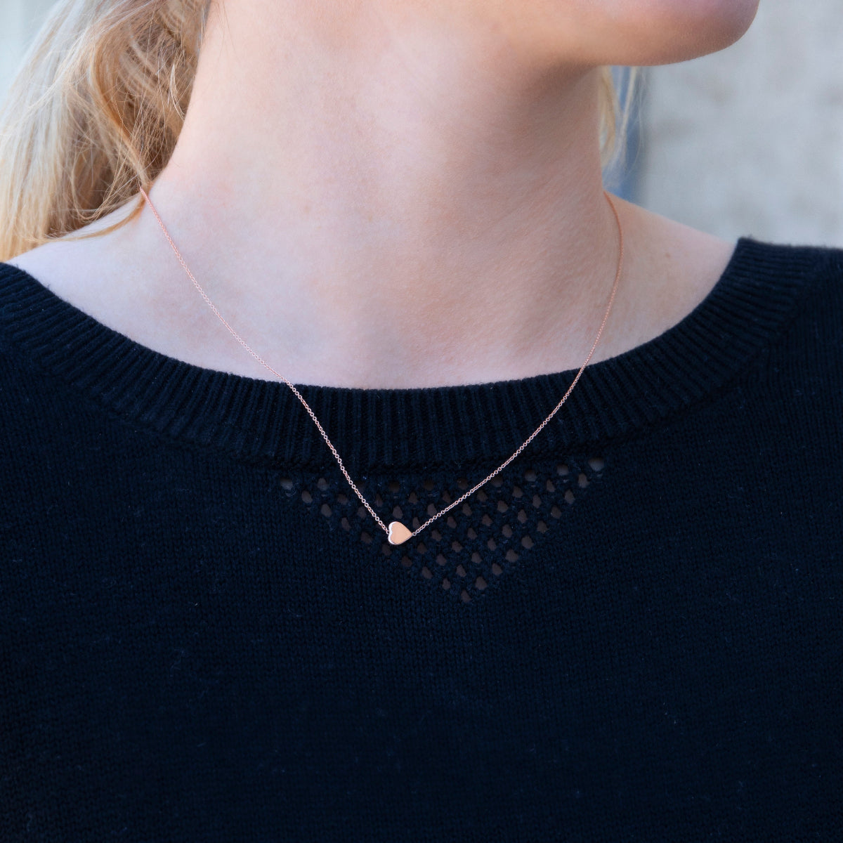 A close-up of a neck wearing a 14k Gold Asymmetrical Charm Necklace - Heart, styled with a navy knit. 