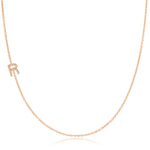A rose gold necklace with a pave letter R charm on a white background. 