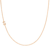 A rose gold necklace with a pave letter S charm on a white background. 