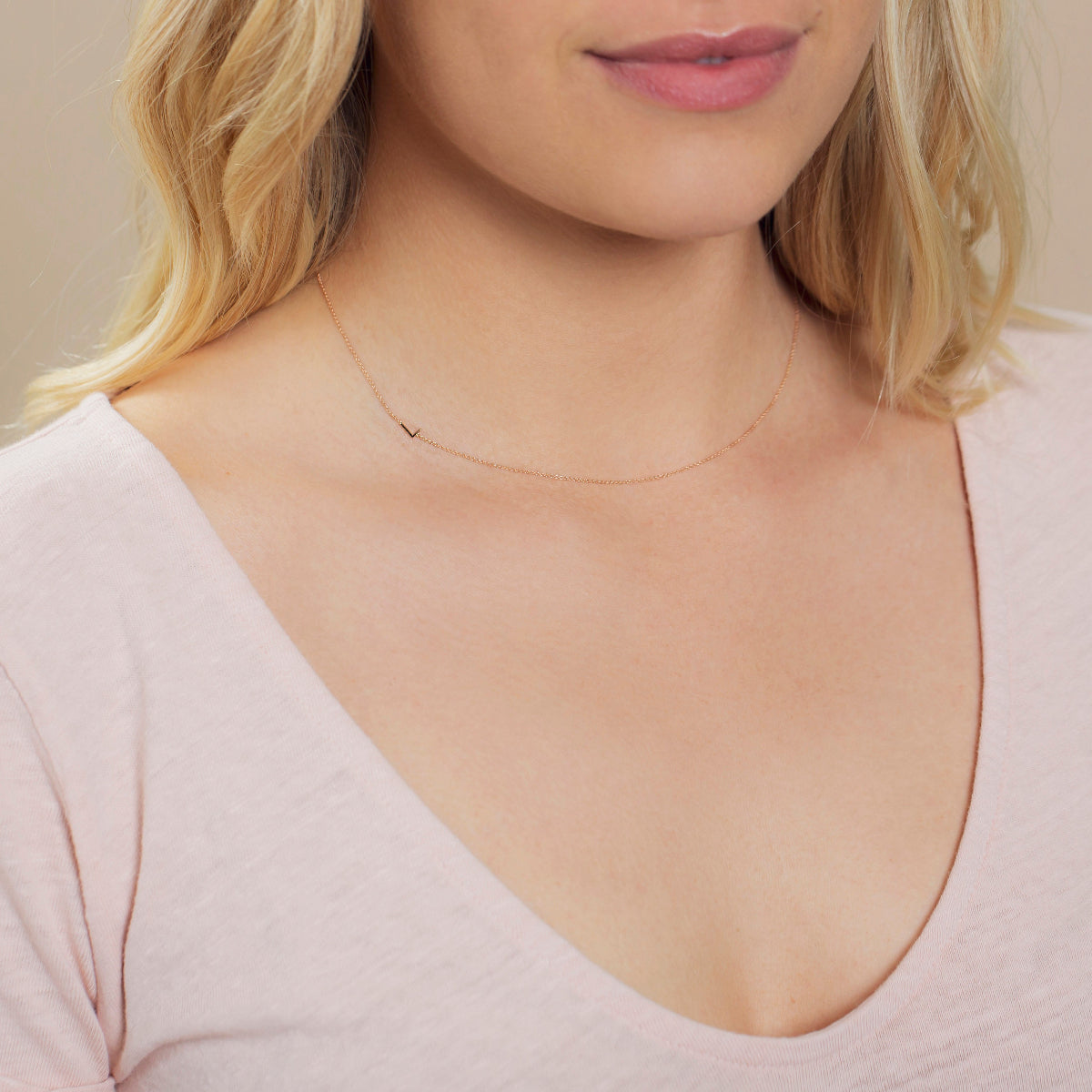 Close-up of a woman's neck wearing a rose gold necklace with a letter L charm. 