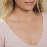 Close-up of a woman's neck wearing a rose gold necklace with a letter O charm. 