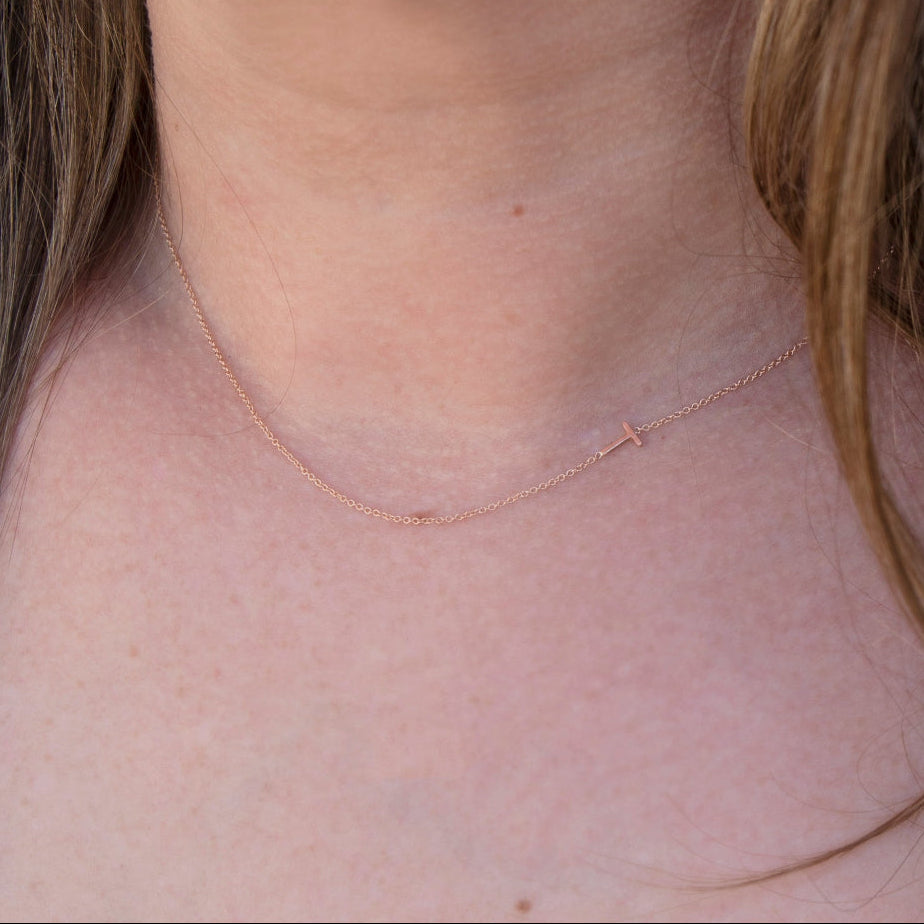 A close-up of a woman's neck wearing a rose gold necklace with a letter T charm. 