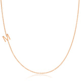 A rose gold necklace with an M letter charm on a white background. 