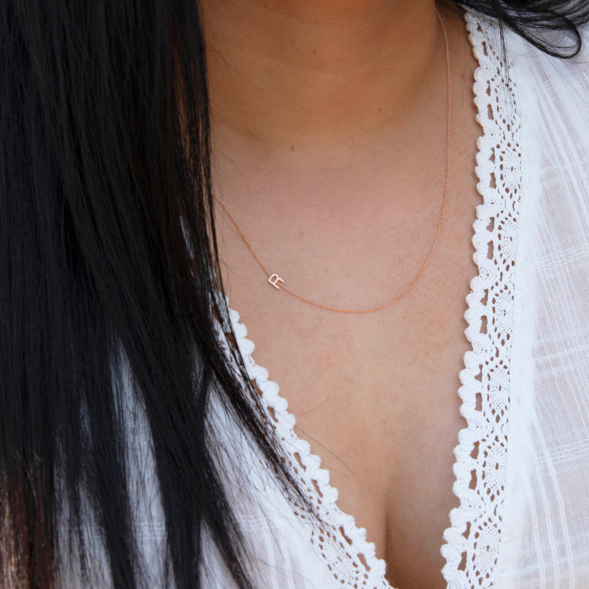 Close-up of a woman's neck wearing a rose gold necklace with a letter R charm. 