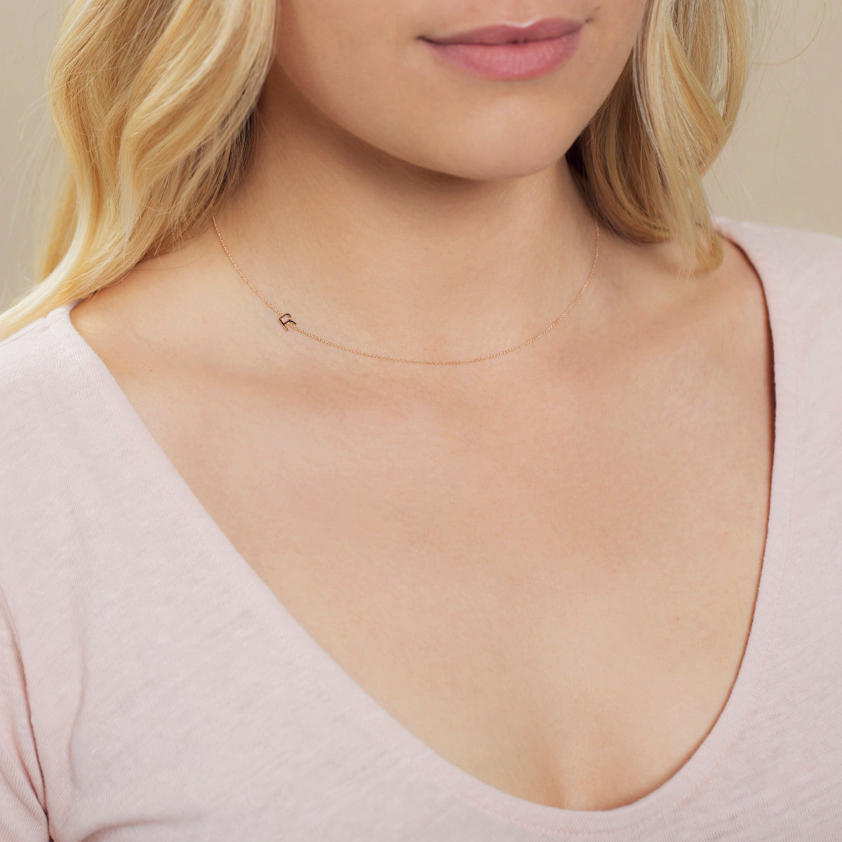 A close-up of a woman's neck wearing a rose gold necklace with a letter R charm. 