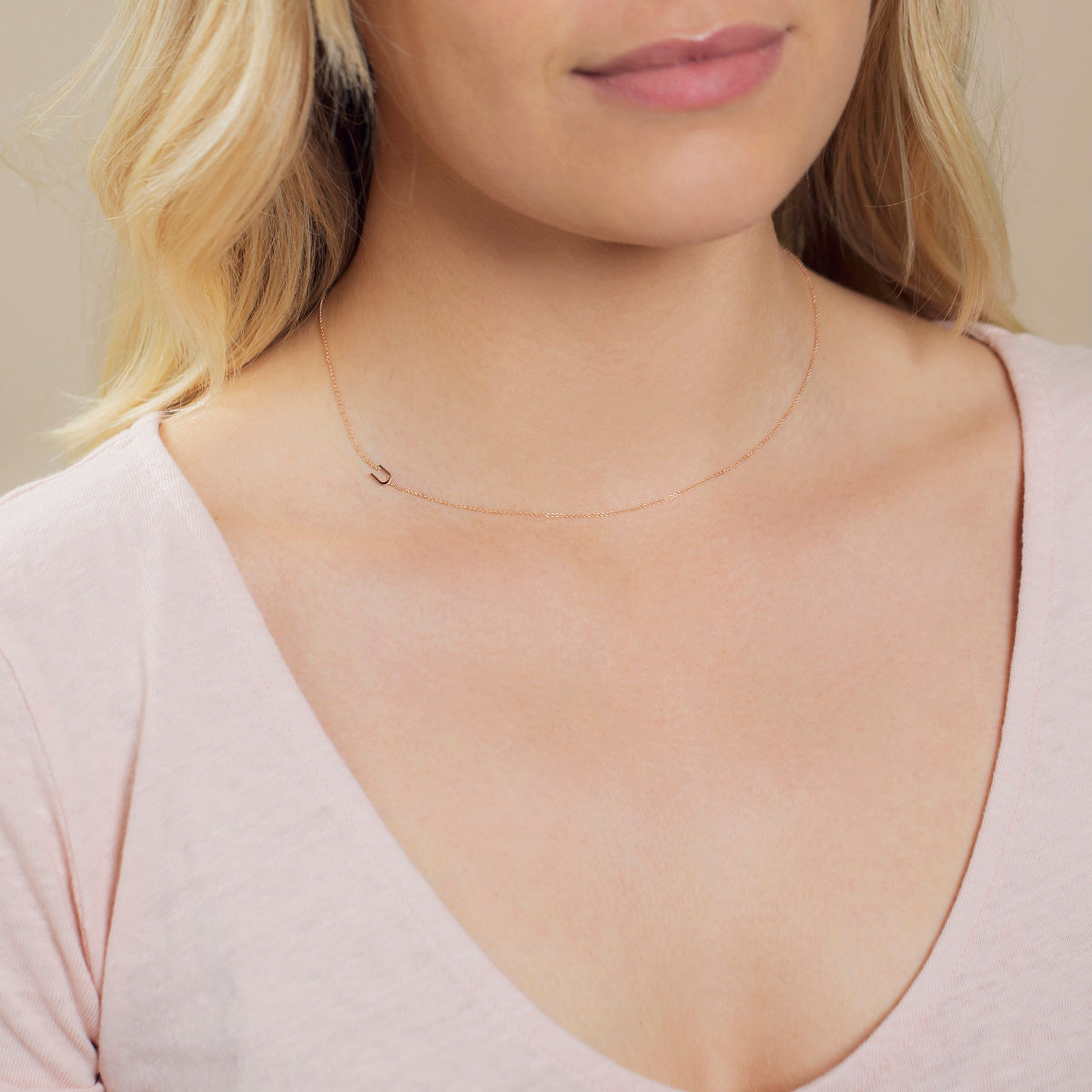 A close-up of a woman's neck wearing a rose gold necklace with a letter U charm. 
