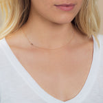 A close-up of a woman's neck wearing a 14k Gold Asymmetrical Number Necklace - 3 in rose gold, styled with blonde hair and a white top.