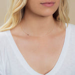 A close-up of a woman's neck wearing a 14k Gold Asymmetrical Number Necklace - 5 in rose gold, styled with blonde hair and a white top.