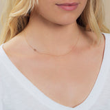 A close-up of a woman's neck wearing a 14k Gold Asymmetrical Number Necklace - 6 in rose gold, styled with blonde hair and a white top.