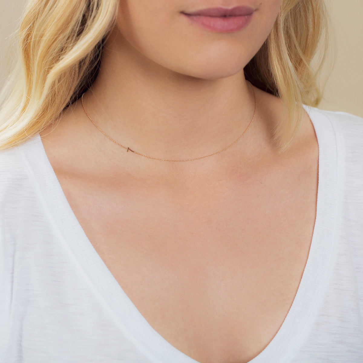 A close-up of a woman's neck wearing a 14k Gold Asymmetrical Number Necklace - 7 in rose gold, styled with blonde hair and a white top.