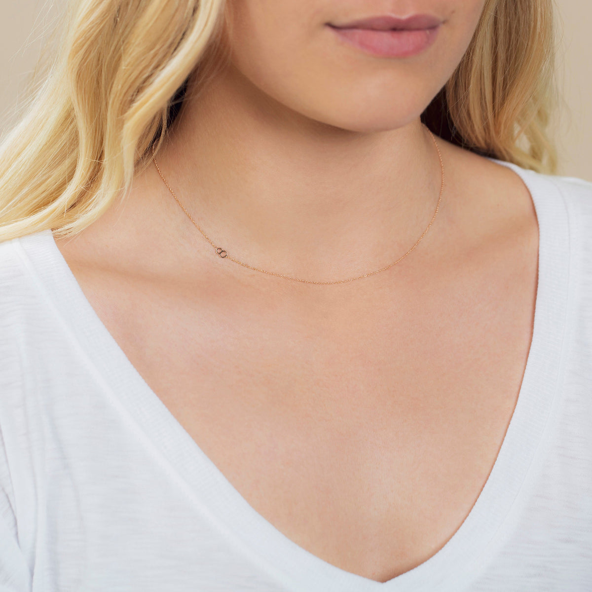 A close-up of a woman's neck wearing a 14k Gold Asymmetrical Number Necklace - 8 in rose gold, styled with blonde hair and a white top.