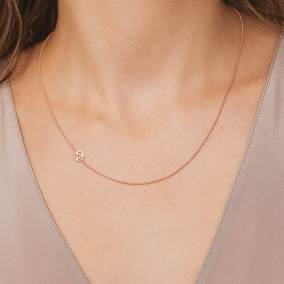 A close-up of a neck wearing a rose gold 14k Gold Asymmetrical Charm Necklace - Recovery with a bead chain, styled with a neutral top.  