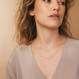 A woman wearing a rose gold 14k Gold Asymmetrical Charm Necklace - Recovery with a bead chain, styled with a neutral top.  