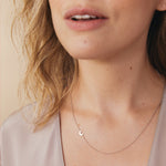 Close-up of a woman's neck wearing a white gold 14k Gold Asymmetrical Charm Necklace - Moon with a bead chain, styled  in a neutral top against a beige background. 