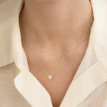 Close-up of a décolletage wearing The Sweetheart Necklace - White Sapphire in white gold with a cream shirt. 