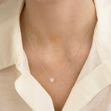 Close-up of a décolletage wearing The Sweetheart Necklace - White Sapphire in white gold with a cream shirt. 