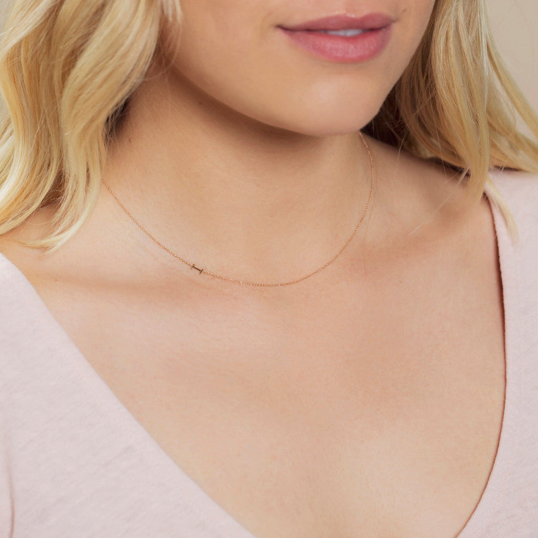 Close-up of a woman's neck wearing a white gold necklace with a letter I charm. 