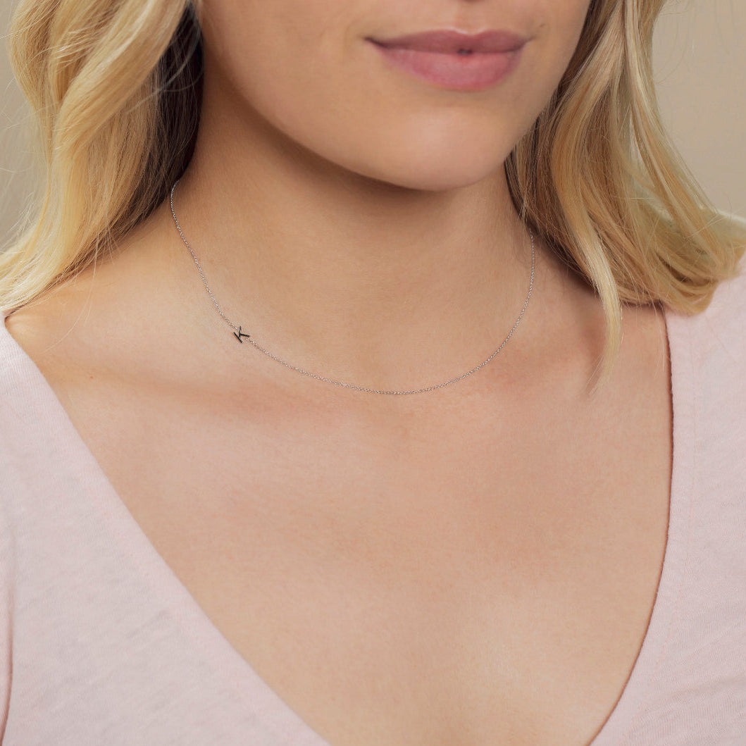 Close-up of a woman's neck wearing a white gold necklace with a letter K charm. 