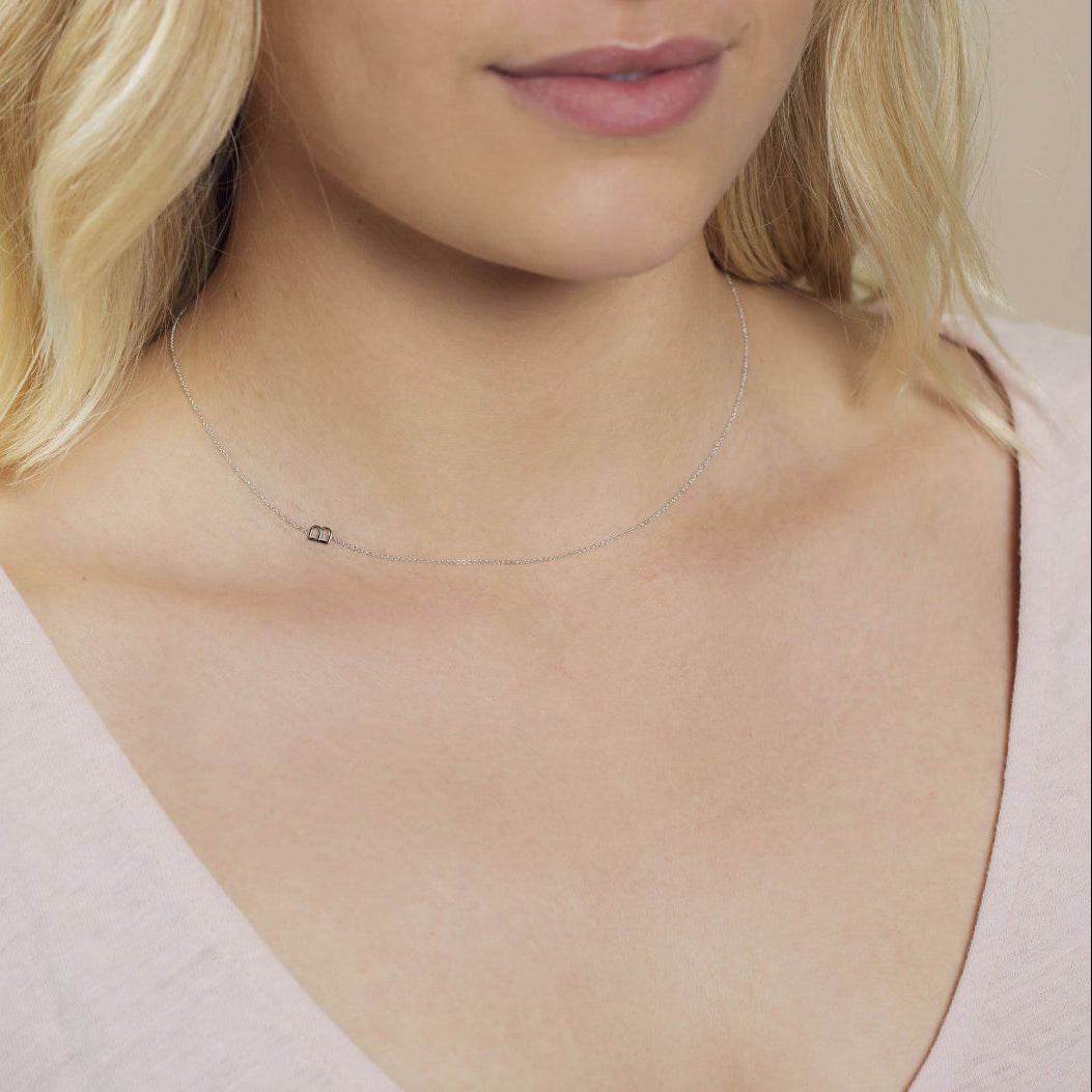 A close-up of a woman's neck wearing a white gold necklace with a letter B charm. 