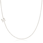 A white gold necklace with an M letter charm on a white background. 