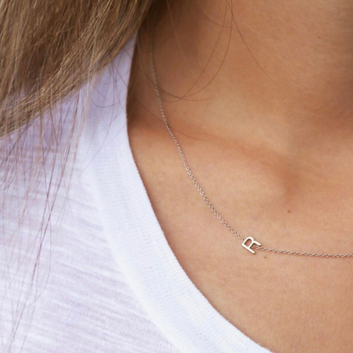 Close-up of a woman's neck wearing a white gold necklace with a letter R charm. 