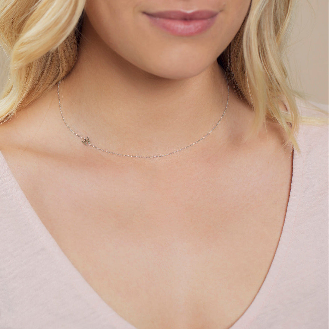 A close-up of a woman's neck wearing a white gold necklace with a letter W charm.