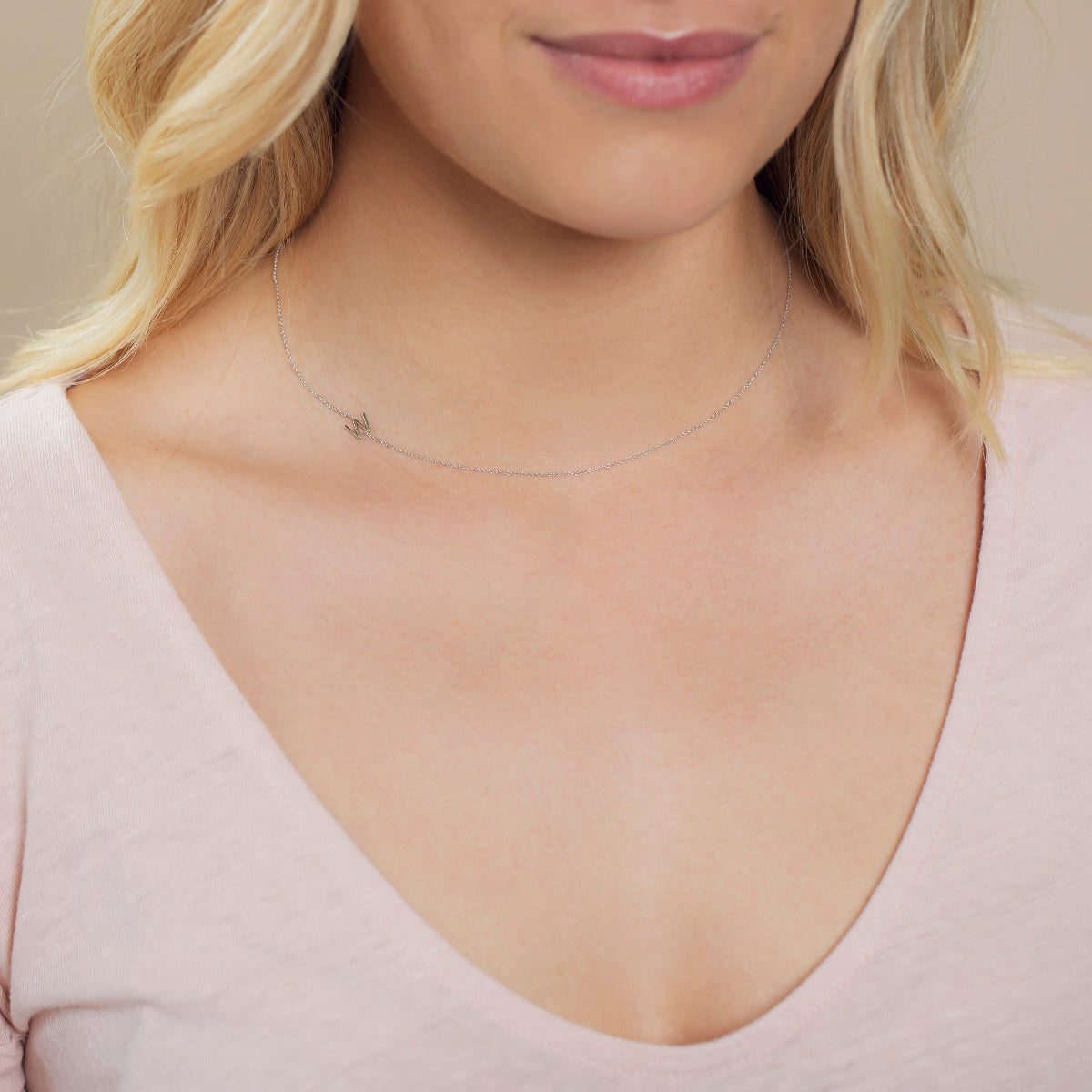 A close-up of a woman's neck wearing a white gold necklace with a letter W charm.