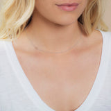 A close-up of a woman's neck wearing a 14k Gold Asymmetrical Number Necklace - 0 in white gold, with blonde hair, styled in a white top.