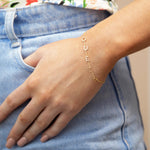 A close-up of a hand wearing a Custom Gold Bracelet – 5 Letters – with the letters Q, U, E, E and N, resting on a blue jean pocket.
