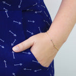 A hand wearing a Straight as an Arrow bracelet in yellow gold, in the pocket of navy blue pants with a white arrow pattern. 
