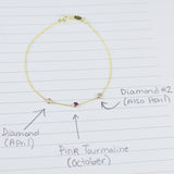 A yellow gold Custom Gold Bracelet with 3 letters and three birthstones (two diamonds and a pink tourmaline) displayed on a sheet of paper with annotations listing the birthstones and their corresponding months.