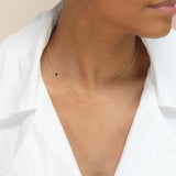 A close-up of a woman’s neck wearing yellow gold 14K Gold Asymmetrical Birthstone Necklace - Onyx (August), styled in a white shirt. 