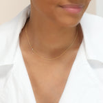 A woman’s neck wearing a yellow gold 14K Gold Asymmetrical Birthstone Necklace - Pearl (June), styled with a white shirt. 
