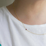 A close-up of a a neck wearing a yellow gold 14K Gold Asymmetrical Birthstone Necklace - Pink Tourmaline (October), styled in a white t-shirt. 