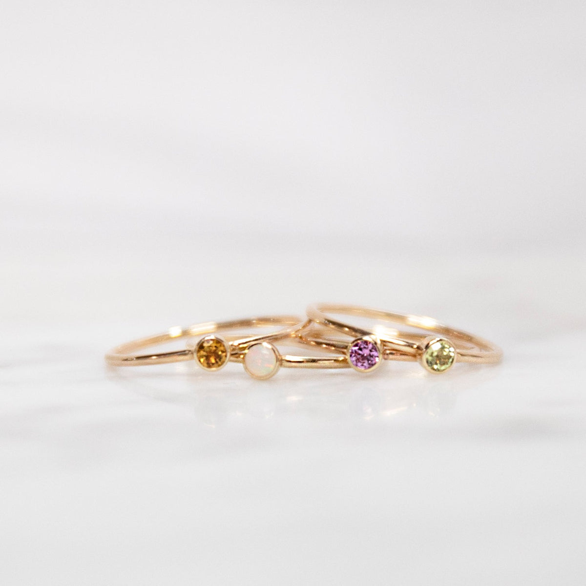 Four yellow gold Birthstone Rings (Citrine, Opal, Pink Tourmaline and Peridot) on a white background. 