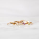 Four yellow gold Birthstone Rings (Citrine, Opal, Pink Tourmaline and Peridot) on a white background. 